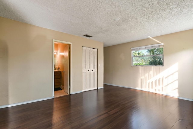 empty room with dark wood-type flooring, visible vents, a textured ceiling, and baseboards