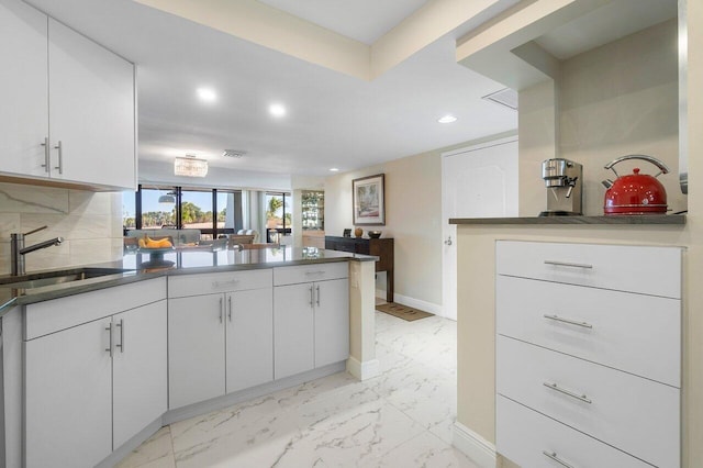 kitchen featuring decorative backsplash, white cabinetry, sink, and kitchen peninsula