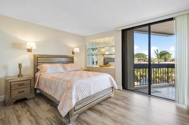 bedroom featuring a wall of windows, wood-type flooring, a textured ceiling, and access to outside