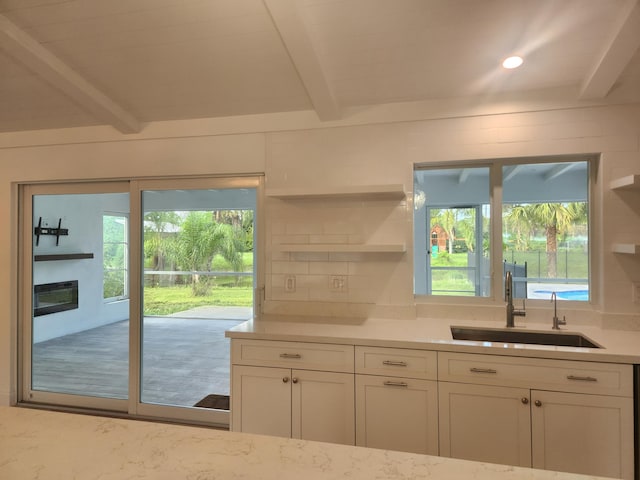 kitchen with beam ceiling, backsplash, white cabinetry, and sink