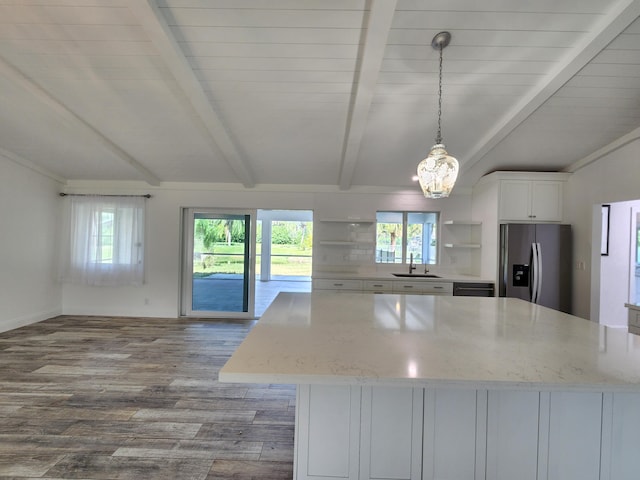 kitchen featuring stainless steel refrigerator with ice dispenser, light stone counters, a healthy amount of sunlight, and beam ceiling