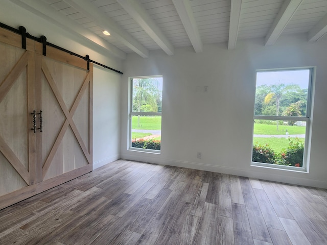 unfurnished room featuring beam ceiling, a barn door, and light wood-type flooring