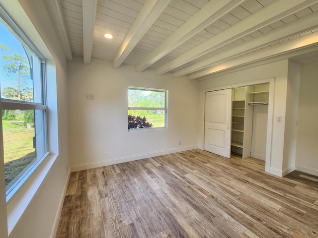 unfurnished bedroom featuring beam ceiling, a closet, and light wood-type flooring