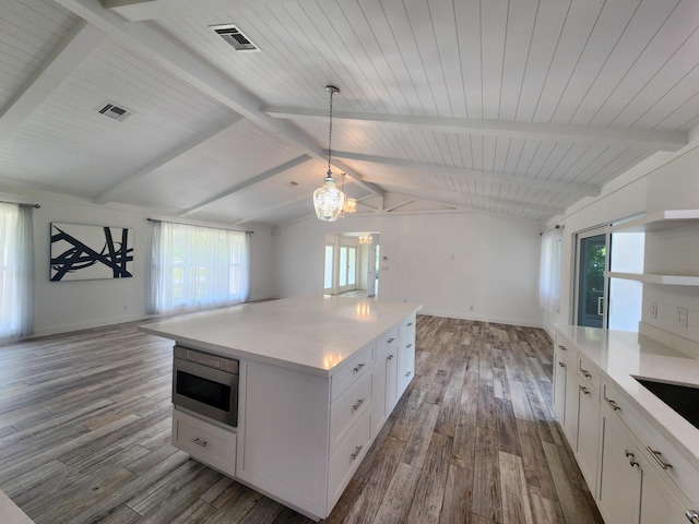 kitchen featuring lofted ceiling with beams, decorative light fixtures, hardwood / wood-style flooring, white cabinets, and stainless steel microwave