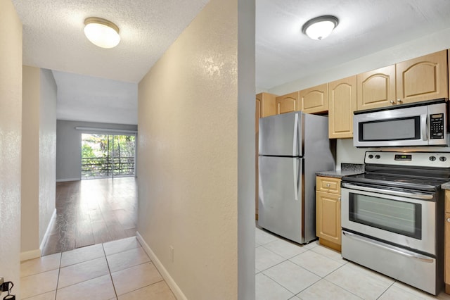 kitchen with light brown cabinetry, a textured ceiling, stainless steel appliances, and light hardwood / wood-style floors