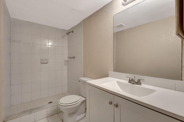 bathroom featuring tile patterned flooring, vanity, toilet, and tiled shower