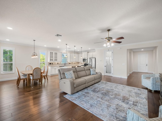 living room with dark wood-type flooring, ornamental molding, ceiling fan with notable chandelier, and a textured ceiling