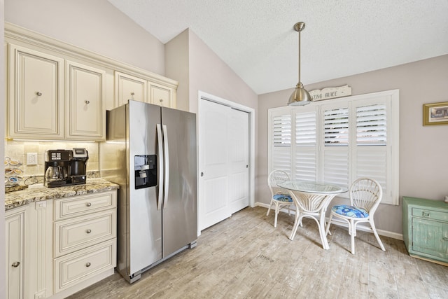 kitchen featuring stainless steel fridge, light stone counters, vaulted ceiling, decorative light fixtures, and cream cabinetry