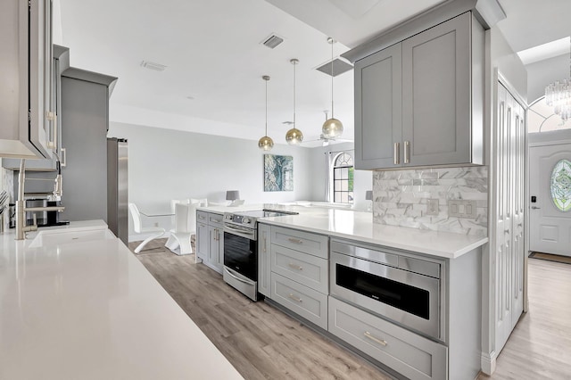 kitchen with tasteful backsplash, pendant lighting, gray cabinets, appliances with stainless steel finishes, and light wood-type flooring