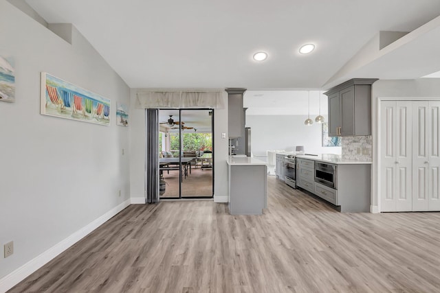 kitchen with light wood-type flooring, backsplash, gray cabinets, hanging light fixtures, and lofted ceiling