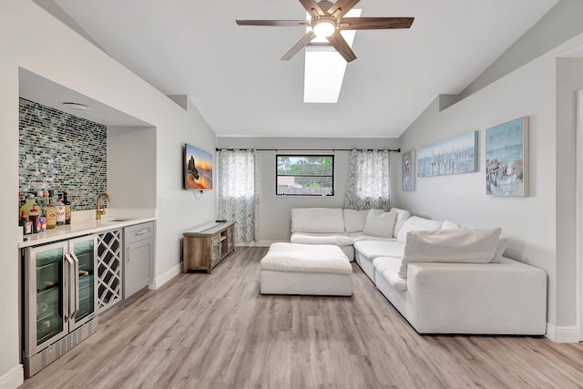 living room featuring vaulted ceiling, ceiling fan, light wood-type flooring, indoor wet bar, and beverage cooler