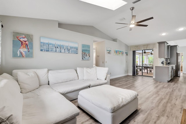 living room with vaulted ceiling with skylight, ceiling fan, and light hardwood / wood-style flooring