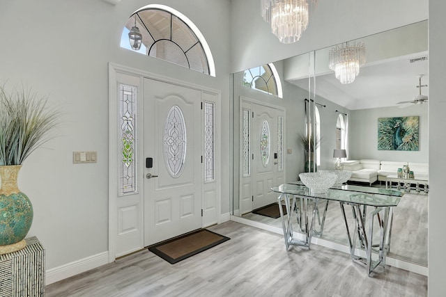 entrance foyer featuring ceiling fan with notable chandelier, light wood-type flooring, and a high ceiling