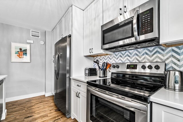 kitchen featuring light wood-type flooring, stainless steel appliances, white cabinetry, and backsplash