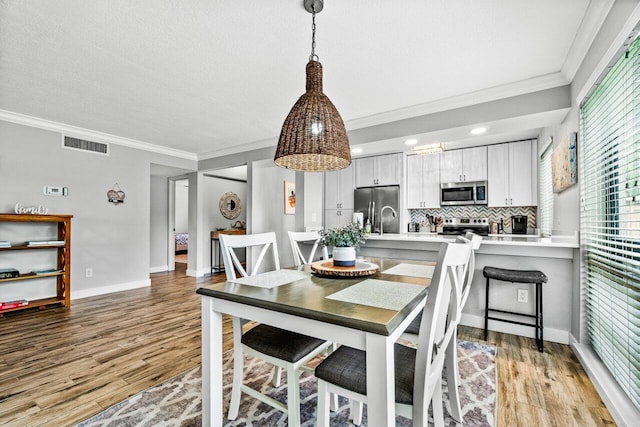 dining space featuring a textured ceiling, light hardwood / wood-style floors, and crown molding