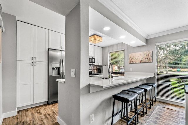 kitchen with white cabinets, appliances with stainless steel finishes, light hardwood / wood-style floors, and a breakfast bar area