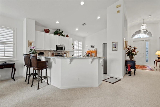 kitchen featuring a kitchen breakfast bar, white cabinetry, light colored carpet, and vaulted ceiling