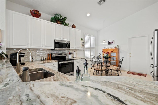 kitchen with appliances with stainless steel finishes, light stone counters, sink, decorative light fixtures, and white cabinets