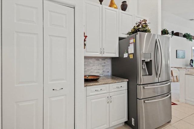 kitchen featuring white cabinets, light stone countertops, tasteful backsplash, light tile patterned flooring, and stainless steel fridge with ice dispenser