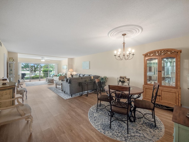 dining area with ceiling fan with notable chandelier, light hardwood / wood-style floors, and a textured ceiling