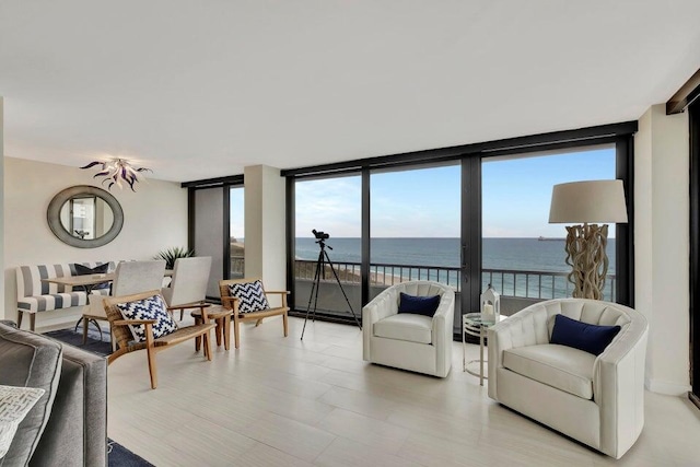 living room with light wood-type flooring, a water view, and a wall of windows