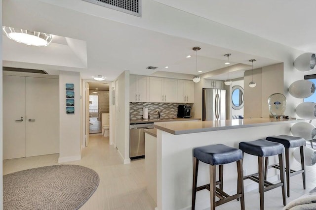 kitchen featuring a kitchen breakfast bar, tasteful backsplash, stainless steel appliances, sink, and decorative light fixtures