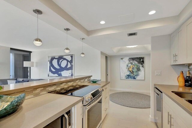 kitchen with appliances with stainless steel finishes, a raised ceiling, white cabinetry, and hanging light fixtures