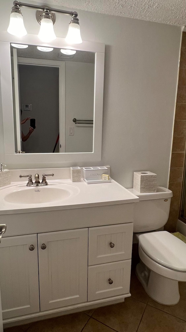 bathroom featuring tile patterned flooring, vanity, toilet, and a textured ceiling