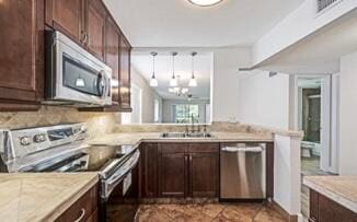 kitchen featuring an inviting chandelier, appliances with stainless steel finishes, dark brown cabinets, light tile patterned flooring, and kitchen peninsula