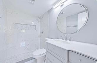 bathroom with tiled shower, vanity, and toilet