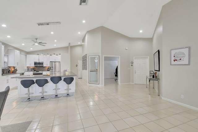 kitchen featuring a center island, white cabinets, light tile patterned floors, appliances with stainless steel finishes, and a breakfast bar area