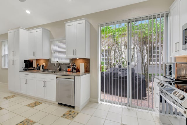 kitchen featuring sink, stainless steel appliances, light tile patterned floors, backsplash, and white cabinets