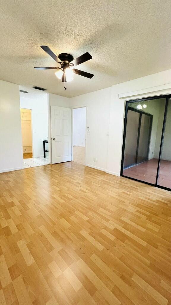 unfurnished room with ceiling fan, a textured ceiling, and light wood-type flooring