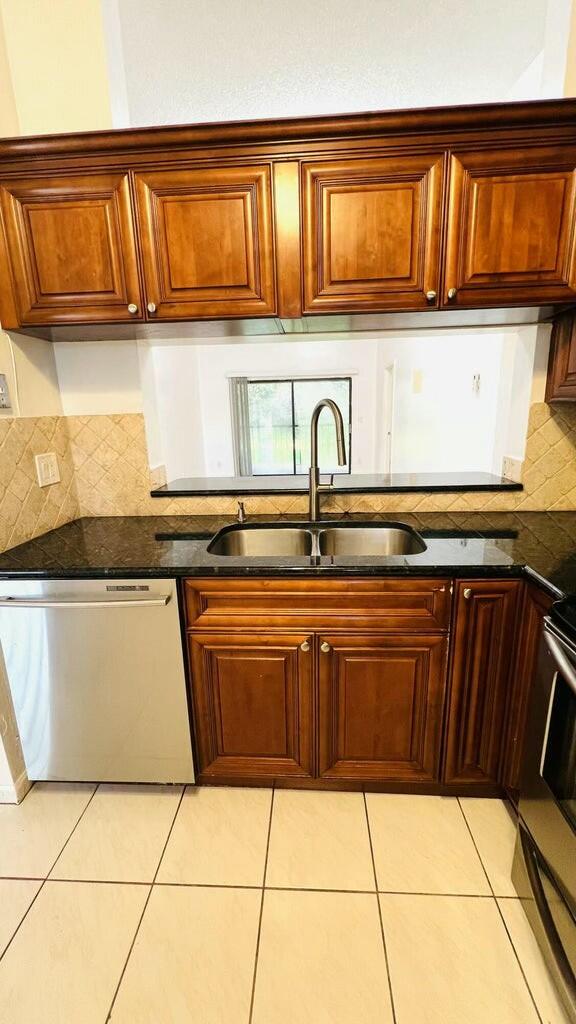 kitchen featuring sink, tasteful backsplash, dark stone countertops, light tile patterned floors, and appliances with stainless steel finishes