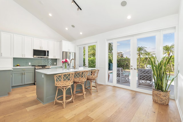 kitchen with french doors, appliances with stainless steel finishes, a center island with sink, white cabinets, and light wood-type flooring