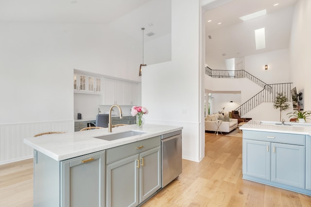 kitchen featuring high vaulted ceiling, a center island with sink, sink, stainless steel dishwasher, and light wood-type flooring