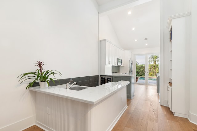 kitchen featuring kitchen peninsula, light wood-type flooring, stainless steel appliances, sink, and white cabinetry