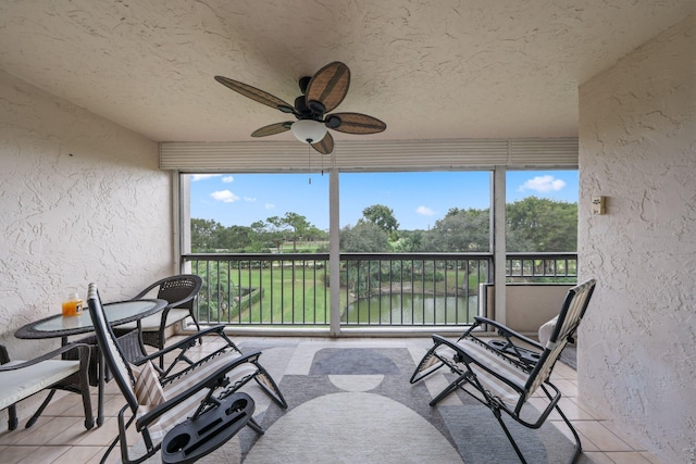 sunroom with ceiling fan and a water view