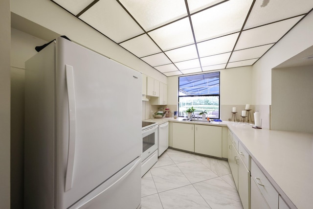 kitchen featuring a paneled ceiling, white appliances, white cabinets, sink, and kitchen peninsula