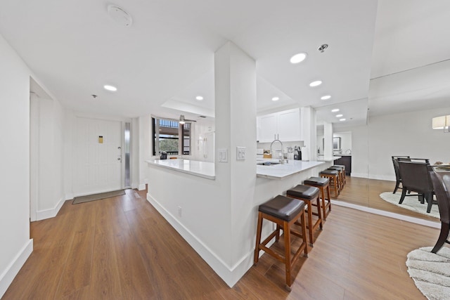 kitchen with a kitchen bar, kitchen peninsula, sink, light hardwood / wood-style flooring, and white cabinetry