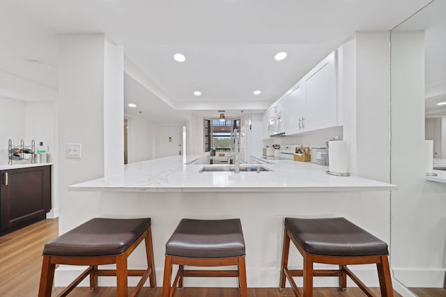 kitchen with white appliances, white cabinets, sink, light wood-type flooring, and kitchen peninsula