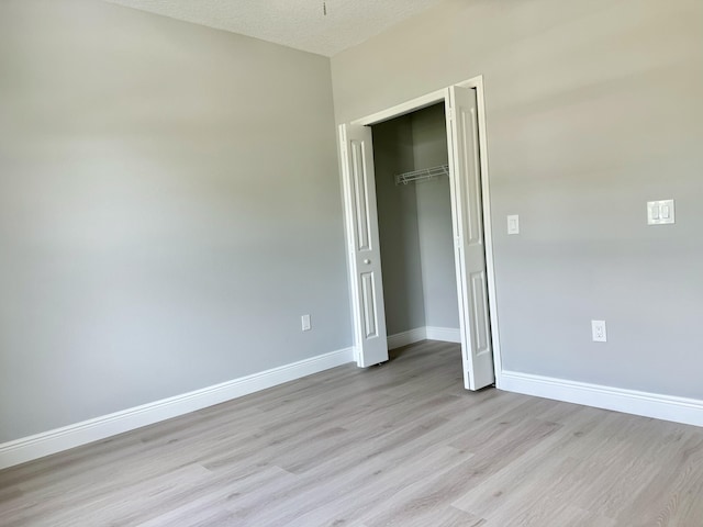 unfurnished bedroom featuring light wood-type flooring, a textured ceiling, and a closet