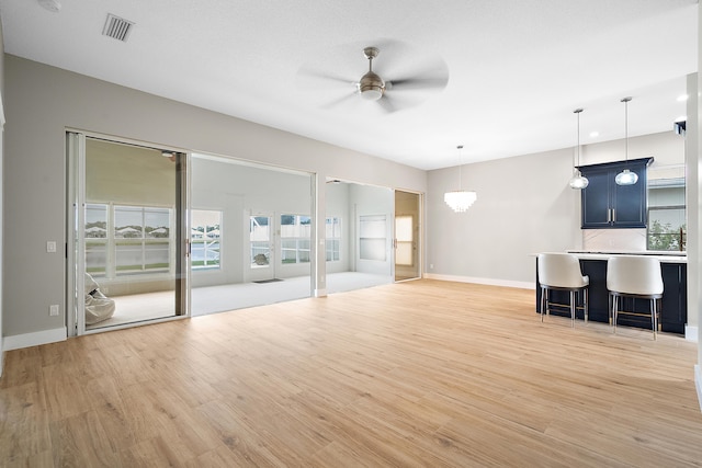 unfurnished living room with ceiling fan with notable chandelier and light wood-type flooring