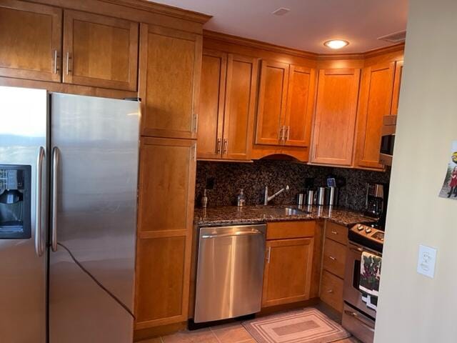 kitchen featuring sink, dark stone countertops, light tile patterned floors, appliances with stainless steel finishes, and tasteful backsplash