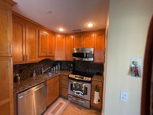 kitchen featuring dark stone counters, appliances with stainless steel finishes, brown cabinetry, and light tile patterned flooring