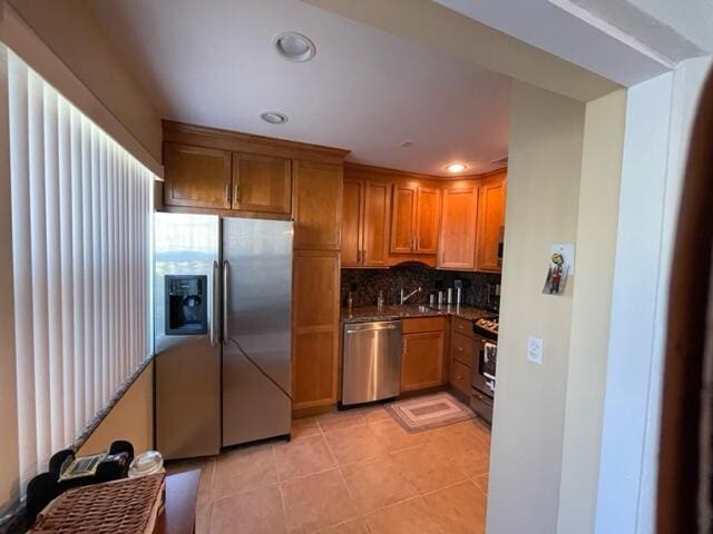 kitchen with light tile patterned floors, decorative backsplash, dark countertops, brown cabinets, and stainless steel appliances