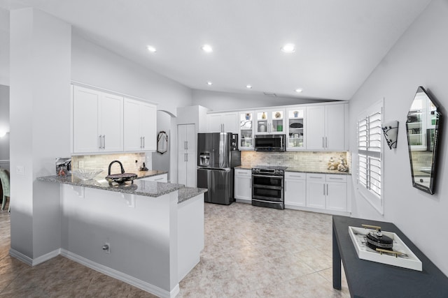 kitchen with stainless steel appliances, kitchen peninsula, stone countertops, vaulted ceiling, and white cabinets