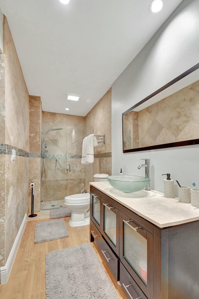 bathroom featuring hardwood / wood-style floors, toilet, a shower with door, vanity, and tile walls