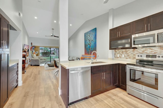 kitchen with kitchen peninsula, appliances with stainless steel finishes, ceiling fan, sink, and light hardwood / wood-style flooring