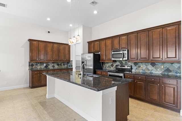 kitchen featuring appliances with stainless steel finishes, backsplash, a kitchen island with sink, and dark stone counters